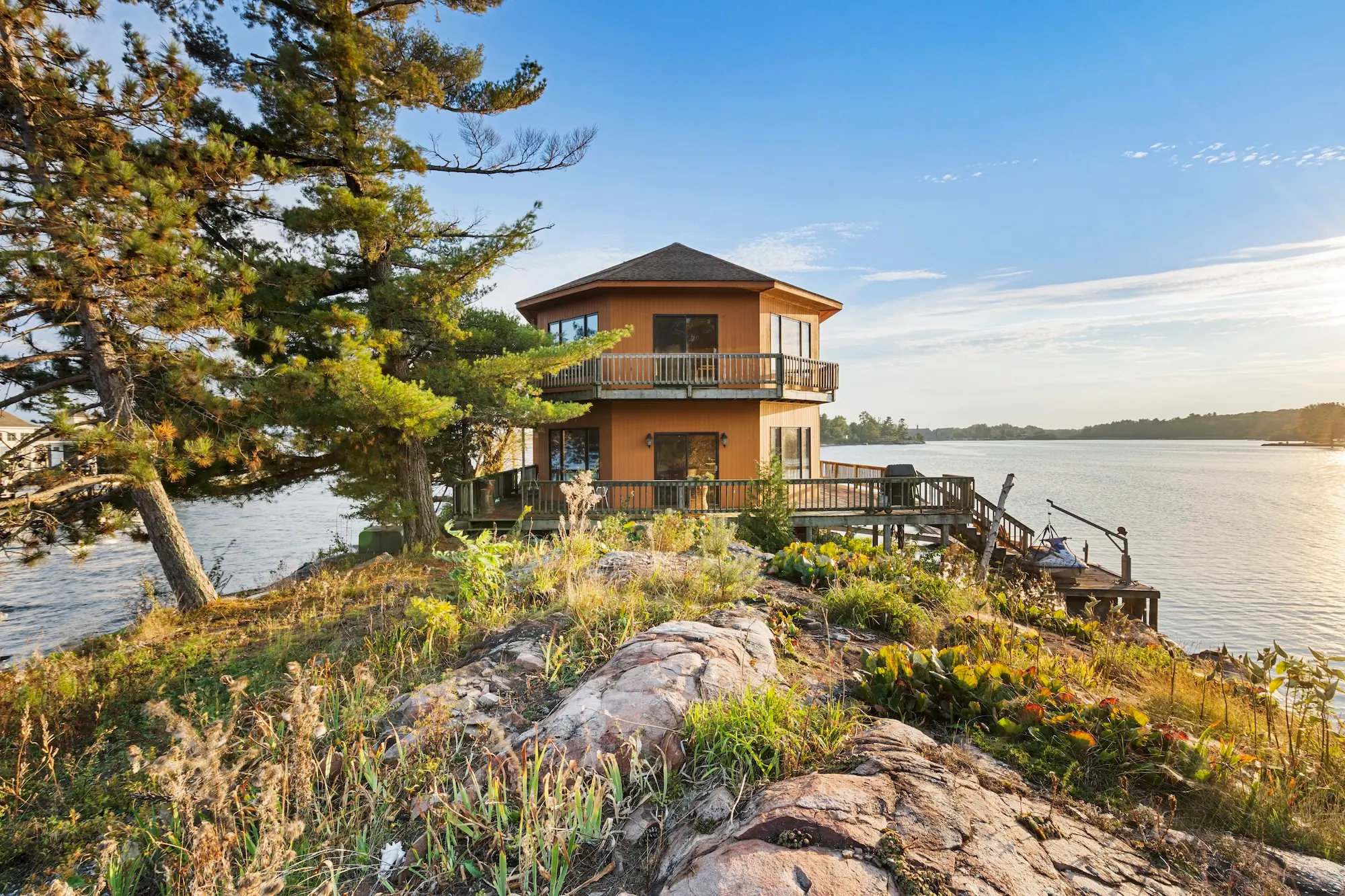 Exterior of the two-storey cedar house on its rocky point with boardwalks, dock and granite outcrops